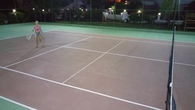 Woman give ball on tennis court and miss back hit at night, mobile phone video.