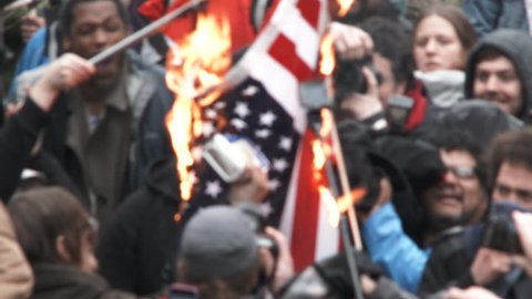 PORTLAND, OREGON - CIRCA 2017: Large group of angry people gather together to burn American flags in protest to Donald Trump taking office.