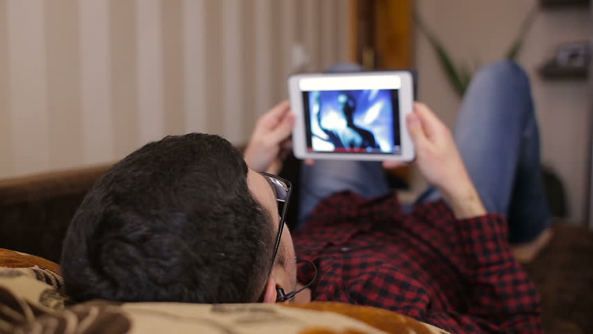 Caucasian man using digital tablet on sofa and listening to music