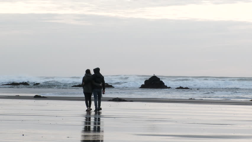 Unrecognizable couple walk and embrace each other at the Oregon Coast.
