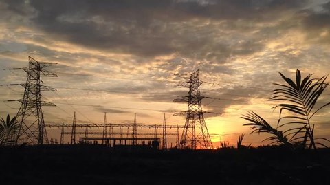 Time-lapse high-voltage electrical distribution substation with pylons and cable lines during sunset