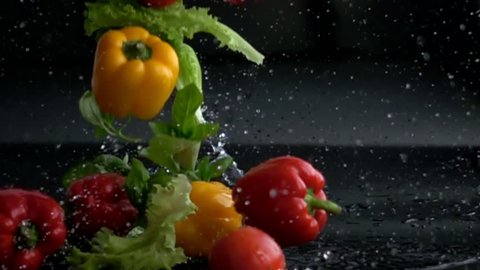fresh vegetables falling with water in slow motion on black background