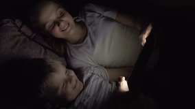 Two kids lying down on the sofa and using tablet pc at night. Slow motion hd video.