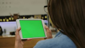 Young attractive woman in glasses watching video on tablet with green screen in the cafe. Close-up. Chroma key. Greenscreen