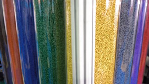 Samples of multi-colored plastic pellets in transparent containers. In the tubes are blue, white, green, red, yellow, pink, grey polymer granules. Shot in motion