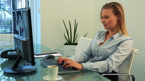 A young, beautiful woman works on a computer in an office