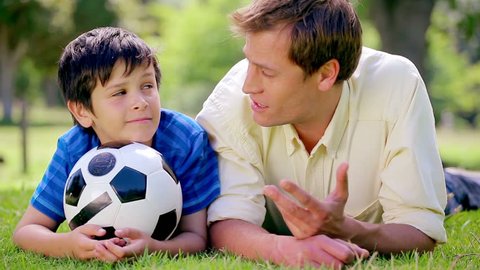 Close up of happy father and son lying on the grass with a soccer ball in the countryside