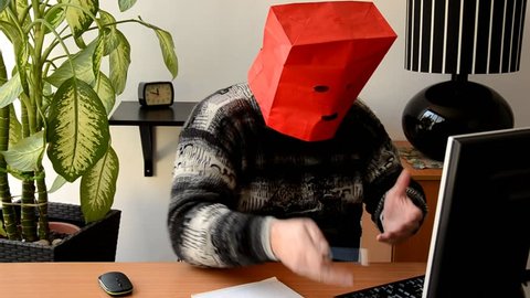 Introverted fat man in red paper bag animatedly speaks with on-line psychologist looking at monitor on the desk. Man needs a psychotherapist but he still hesitates to open his face