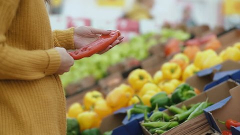 Close-up view of woman s hand choosing a red pepper in the supermarket, holding some. Showcase with vegetables. 4K