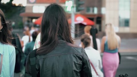 Young brunette woman crossing street in the city, hair fluttering in the wind. Slow motion, steadicam shot, back view.