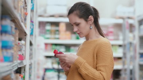 Young beautiful woman standing in front of baby food shelves, holding packaging baby food, choosing best. 4K