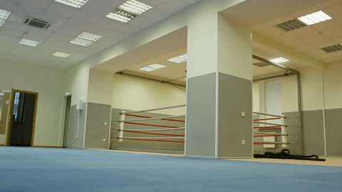 Low angle tracking shot of empty gym with boxing ring for training