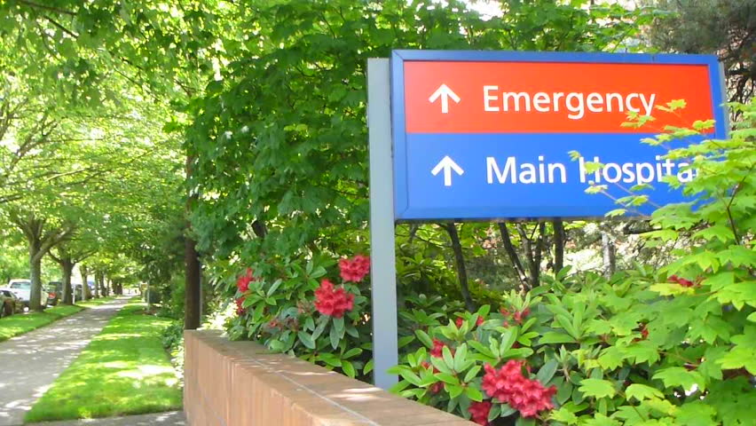 Person walks by sign that reads Main Hospital and emergency ahead near hospital.