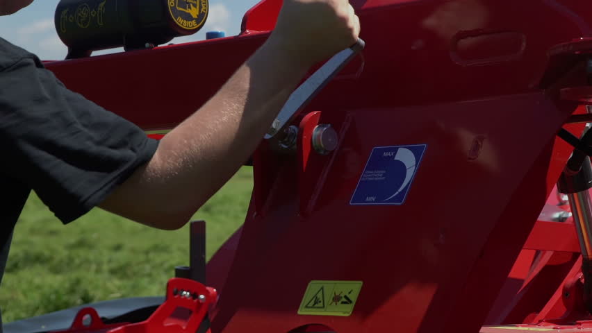 A young farmer is winding up the handle on a grass cutting machine to adjust the device.