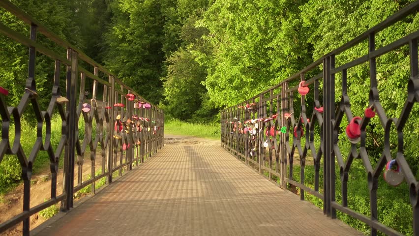 Beautiful little girl goes on bridge with attached locks in summer city park.