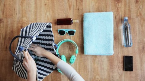 summer holidays and people concept - hands packing beach accessories, smartphone and headphones with bottle of water to bag