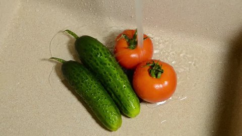 Wash vegetables in a ceramic sink. Fresh tomatoes and cucumbers under running water