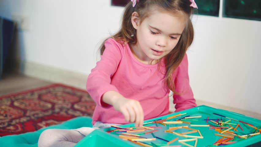 Girl playing with colorful wooden sticks on the floor. Medium shot.