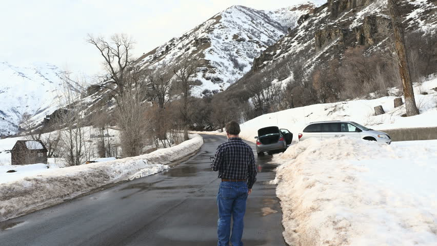 Man lands drone on wet snow lined blacktop mountain road
