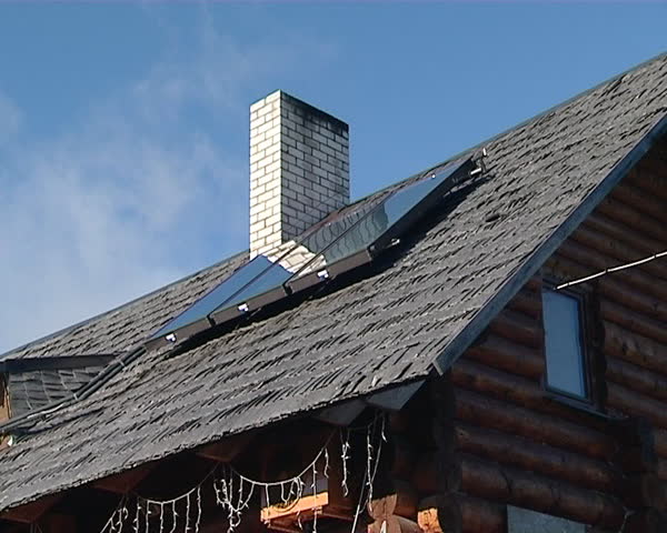 wooden log homestead house and solar collectors on roof. clouds in sky.