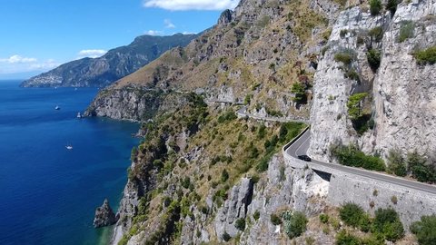 Aerial flying past beautiful coastline car driving over cliff road in front of drone amazing Mediterranean landscape and automobile driver maneuvering flexible on curvy ocean road summer vacation 4k