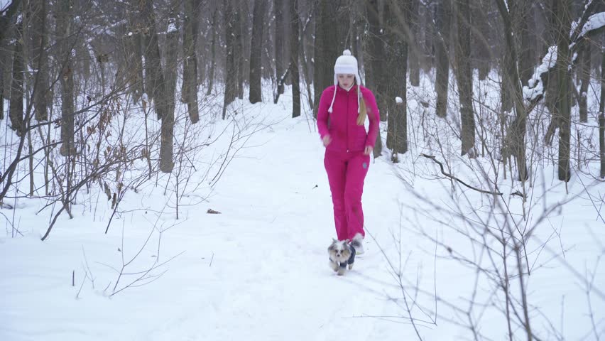 Young blonde woman running in snowy forest with small dog