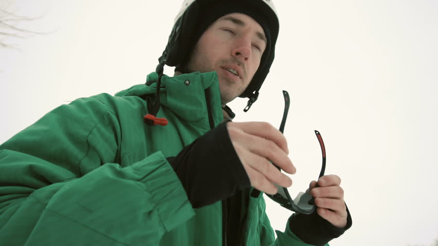 Young attractive snowboarder man in green suit wears black sunglasses