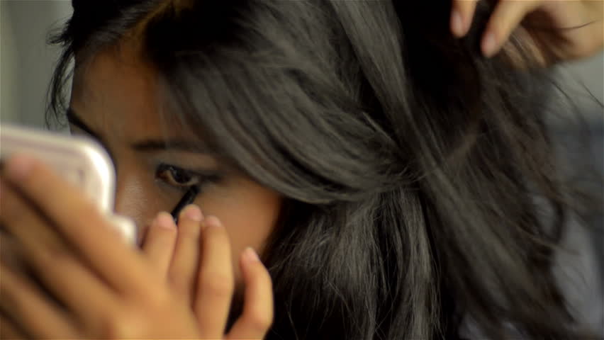 Young Asian woman looking into a mirror while getting her hair and makeup done.