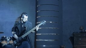 Professional stylish rock guitarist playing on bass  guitar with emotions on dark background with strobe lights in slow motion 200 FPS .  Shot on RED HELIUM Cinema Camera.