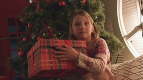 Close up of hands of little girl hanging holiday decorations on beautiful snowy Christmas tree in home interior. Point of view real time full hd video footage.