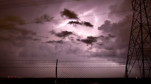 Huge thunderstorm storm with extensive lightning, framed by an electrical tower and barbed wire fence. There is also a funnel cloud forming in the lower-right. HD 1080p time lapse.