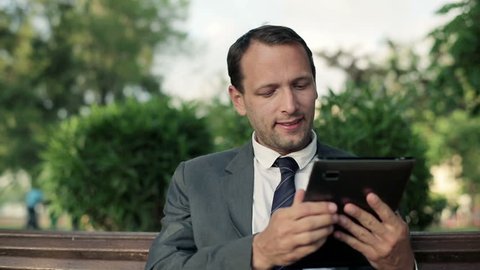 Young businessman working on tablet computer in the park, dolly shot
