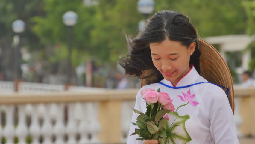 Vietnam girl in the national costume and dress Ao Dai posing and smiling for the camera. In the hands holding a pink rose.