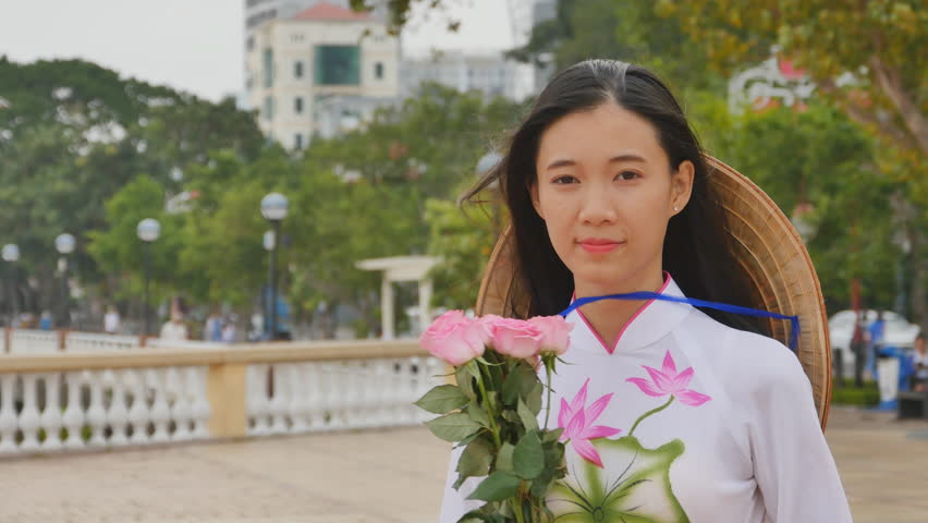 Vietnam girl in the national costume and dress Ao Dai posing and smiling for the camera. In the hands holding a pink rose.