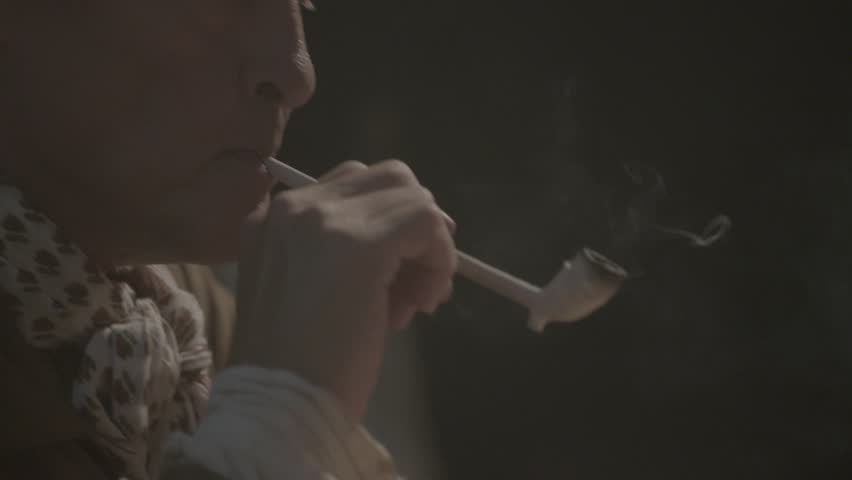 VIRGINIA - OCTOBER 2016 - SLOW-MOTION Reenactment, American Revolutionary War 18th & 17th century era recreation -- Man holds Tavern pipe and smokes by candle & fireplace light in saloon. Tobacco.
