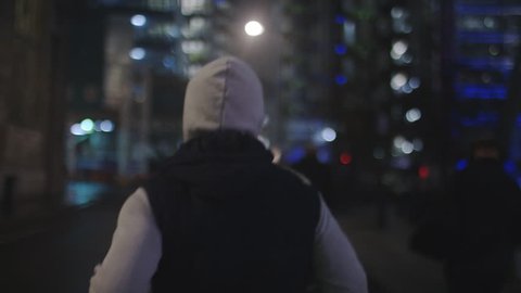 4K Camera follows a man running in the city at night, in slow motion 