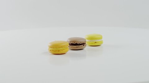 Three colourful macarons are rotating together on the white surface