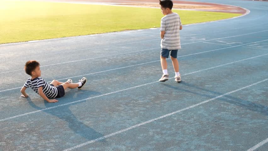 Young Asian boy running on blue track, fall and help by another boy. Royalty-Free Stock Footage #23952340