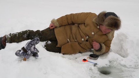 Fisherman catches a fish on ice fishing and drinking hot tea from a thermos