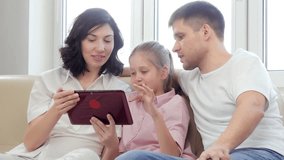 Family using digital tablet. Parents showing digital tablet to their daughter at home.