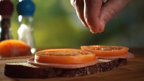 Man is adding some salt on the sandwich, close-up slow motion video