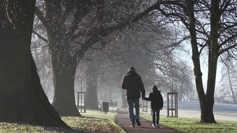 Father and Son walking away from camera through English country park on Winter's morning.