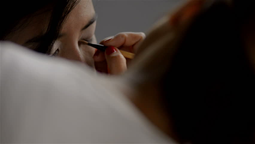 Makeup artist applying eyeliner to the eyes of an Asian woman.