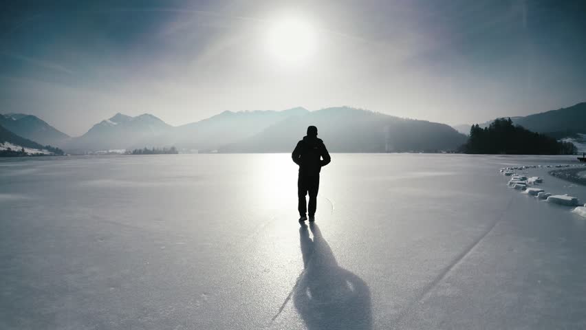 Lonesome man walking on frozen lake schliersee, bavaria, germany, near munich against mountains