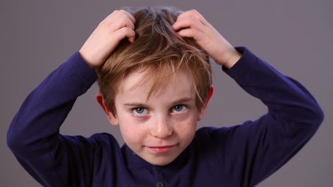 thinking cute small male preschooler with freckles and red hair scratching his head for reflection or skin itching, grey background, indoors