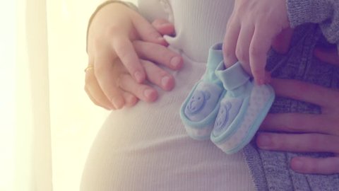 Pregnant Happy Woman holding Blue Baby Shoes in her Hands. Mom and dad Expecting Baby. Pregnant Woman Belly. Pregnancy. Happy parents. Baby Shower. Slow motion 240 fps, high speed camera HD 1080p