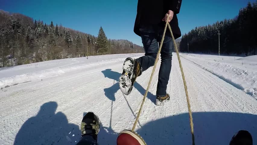 Dad pulling a sledge during a sunny winter day. Slow motion
