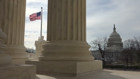 WASHINGTON, DC - FEB. 2017:  U.S. Supreme Court faces the Capitol, Senate and American flag.  Through pillars of front portico the close by US Capitol building can be seen.