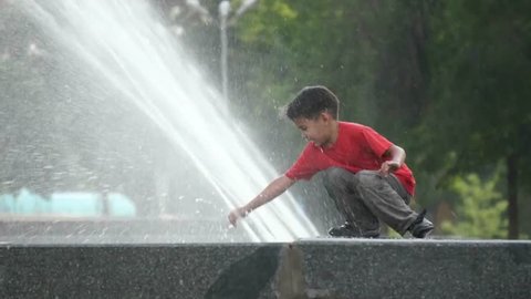 Boy touching a fountain on a summer day. 