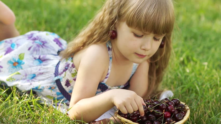 Child eating cherries lying on the grass
